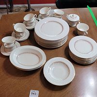 Wide shot showing multiple cups with saucers, stacks of dinner plates and salad plates, serving bowls, creamer and sugar bowl with lid.