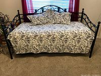 Fully assembled daybed with floral comforter and two pillows against a window.