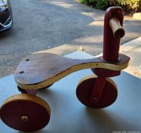 Wooden antique ride-on tricycle toy showing seat, wheels, and handlebars outdoors.