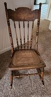 Full view of the antique wooden rocking chair showing carved backrest and cane seat.