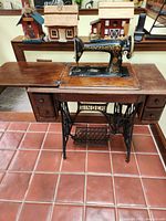 Full front view of the antique Singer sewing machine in its wooden cabinet with drawers and treadle base.