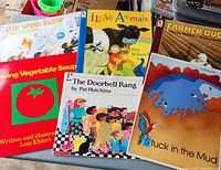 Photo showing six large children's books arranged in a pile. Titles visible are The Wind Blew, I Love Animals, Farmer Duck, Making Vegetable Soup, The Doorbell Rang, and Stuck in the Mud.