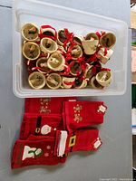 Top view showing numerous ceramic dog-themed Christmas teacup ornaments with red ribbons arranged in a bin. Below the bin are six red holiday finger towels with various Christmas motifs including Santa and snowman.