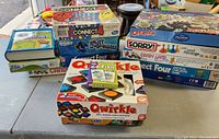 Photo showing a variety of children's games including Connect Four, Qwirkle, Go Fish card game, Memory, and others stacked on a table.
