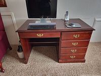 Wood computer desk with dark finish, four drawers with brass handles on the right, and a closed cabinet door on the left. Keyboard, mouse, and phone on top.