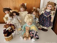Photo showing all seven dolls arranged on a table including one in a maroon and gold costume and two holding plush toys