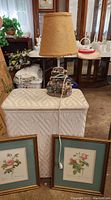 Photo showing the wicker hamper, floral resin lamp, and two framed botanical pictures in a room with other furniture and decor items.