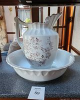 Photo showing white ceramic pitcher with floral design and matching wash bowl on counter, no visible chips or cracks.
