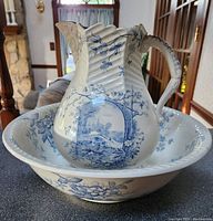 Photo of vintage white ceramic pitcher inside matching bowl, both decorated with detailed blue floral and scenic designs, placed on tabletop