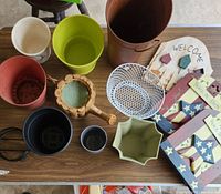 Overview photo showing various garden pots, a wire basket, a wooden watering can décor, and painted wooden garden signs, plus a welcome plaque.