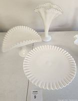 Seven pieces of vintage Fenton milk white glassware on table, showing ruffled edges and opaque white color.