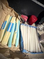 Photo showing multiple tall taper candles in pale yellow and blue, some still in wrappers