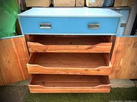 Front view of open dresser showing one blue painted drawer and three cedarwood drawers inside two cabinet doors.
