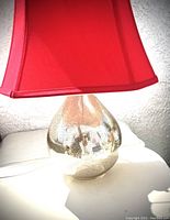 Close-up of one crackled silver glass lamp base with red satin lampshade attached, showing teardrop shape and reflective crackled texture.