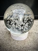 Front view of clear glass crystal ball with multiple internal air bubbles on a white stand.