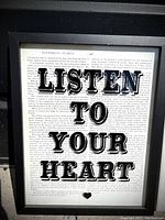 Close-up photo of framed print 'LISTEN TO YOUR HEART' showing vintage book page background with black text and small heart graphic.