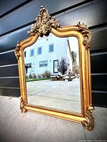 Front angle view showing entire ornate gilt mirror with Baroque style crest and detailed carving.