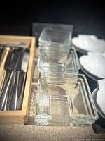 Photo showing stacked square clear glass dessert bowls and white ceramic shell-shaped server plates.