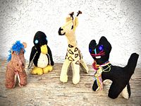 Four handmade stuffed animals set: donkey, penguin, giraffe, and cat against a white wall and wooden surface