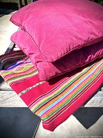 Two bright deep pink pillows stacked on a wooden surface on top of the red tapestry with multicolored stripes