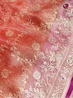 Close-up of pink-orange sari fabric with gold embossed floral patterns and gemstones.