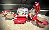 Wide view of red KitchenAid mixer, stainless steel bowls, textiles, tray, ceramic and glass bowls