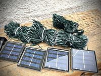 Four coiled 20m dark green string light sets and four solar panels arranged on wooden surface.
