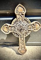 Close up of ornate carved decorative cross with metal filigree centerpiece, showing intricate pattern and aged finish.
