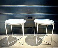 View of both off-white metal round tray tables side by side showing round removable tops and metal bases.