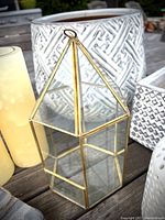 Close-up of the brass and glass geometric lantern with large ceramic planter in background