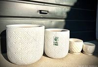 Four white ceramic planters displayed in a row; two large ones with diamond pattern, smaller two with textured patterns including owl.
