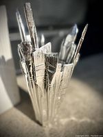 Close-up photo of the silver-tone vase featuring sculptural paintbrush shapes showing detailed brush tips and textured handles.