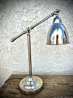 Photo of vintage chrome desk lamp on wooden surface against textured white wall