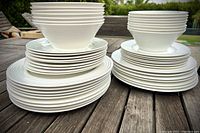 Stacked dinner plates, salad plates, and bowls viewed from the side on a wooden table showing quantity and style.