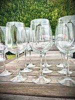 Ten large clear wine glasses with long stems arranged on a wooden surface.