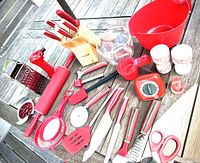 Overhead photo of the full kitchen tool set on outdoor table, showing all items including knives in block, timer, rolling pin, graters, peelers, scissors, spatula, measuring cups, and other accessories in red and wood.