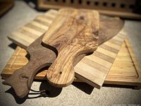 Stack of wooden cutting boards and platters showing natural wood grain patterns and handles with holes for hanging.