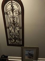 Photo showing the full view of the two wall art pieces: tall arched metal and wood decorative panel and smaller wooden framed egret print below it.