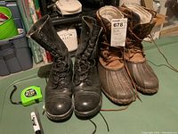 Black leather combat boots next to brown duck boots with measuring tape and marker beside them for scale.