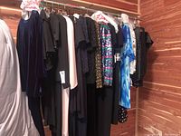 Wide view of the lot of women's evening and cocktail dresses hanging, showing various colors and styles including velvet, sequins, and prints.