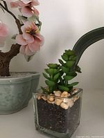 Glass and jadeite bonsai tree with pink flowers and faux succulent in a clear glass pot with soil and pebbles