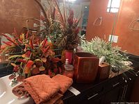 Full view of copper towels, faux floral arrangements, copper trash can and tissue box, candle, soap, and bath cups on bathroom counter