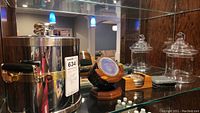 Photo showing stainless steel ice buckets with handles, decorative glass jar, wooden holder with round metal coasters, and square stone coasters.
