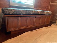 Front and side perspective showing overall chest and cushion under window in wood-paneled room