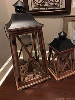 Two wooden lanterns with black metal tops sitting on a floor, showing their overall size and style