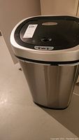 Front and top view of stainless steel motion sensor trash can with black lid and control buttons.