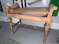 Full view of wooden piano bench showing carved legs and armrests, seat surface is wooden and worn