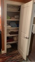 Shelving unit with folded and stacked linens including blankets, quilts, and pillows.