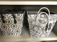 Four fabric storage baskets on a shelf; two gray and cream geometric pattern with black handles, two gray and cream floral damask pattern with white handles.