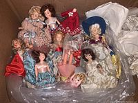 Full view of the box containing multiple vintage plastic dolls in various dresses and conditions, some showing damage.